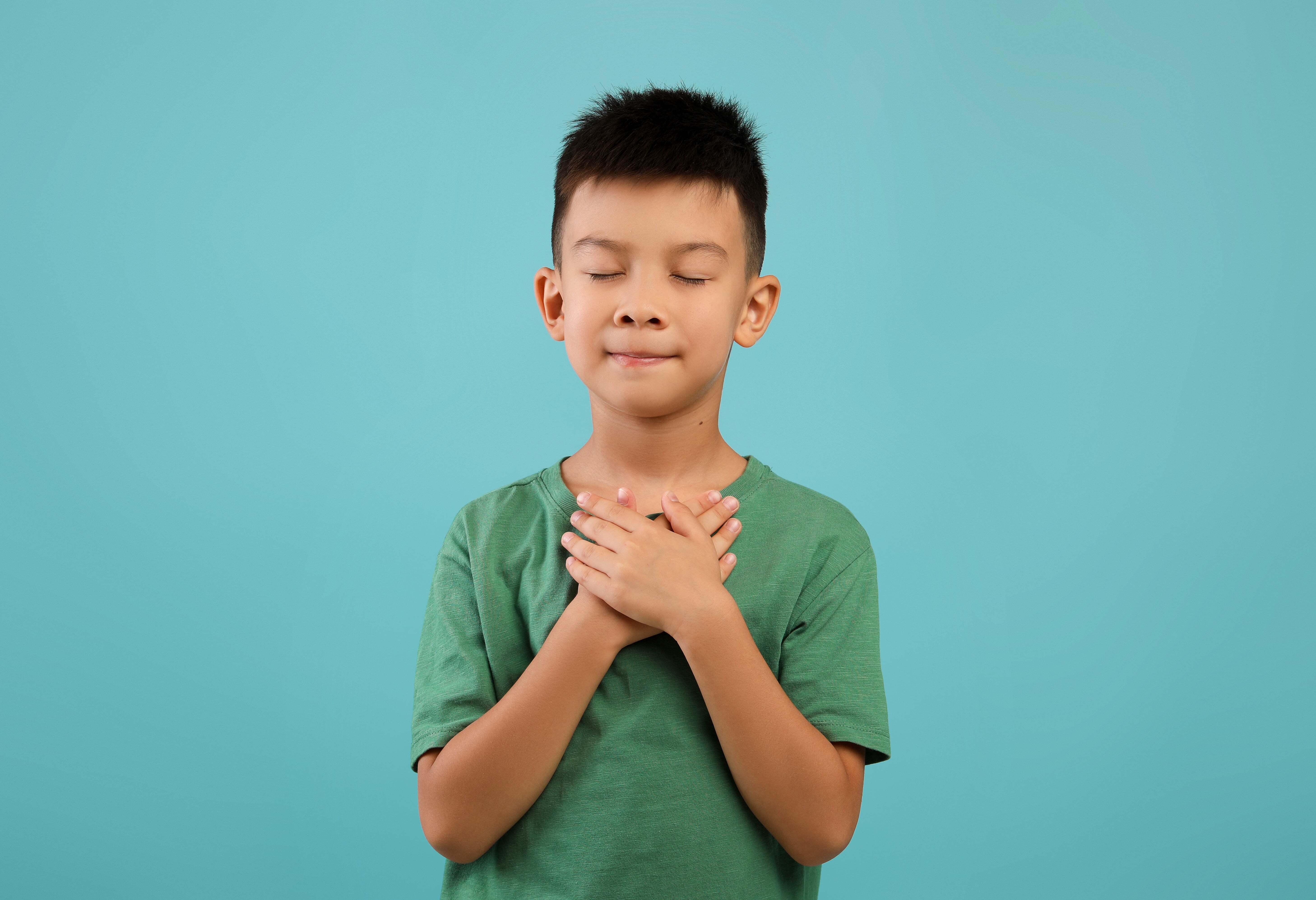 A young boy placing his hands over his chest with his eyes closed, practicing mindfulness and gratitude activities for kids.