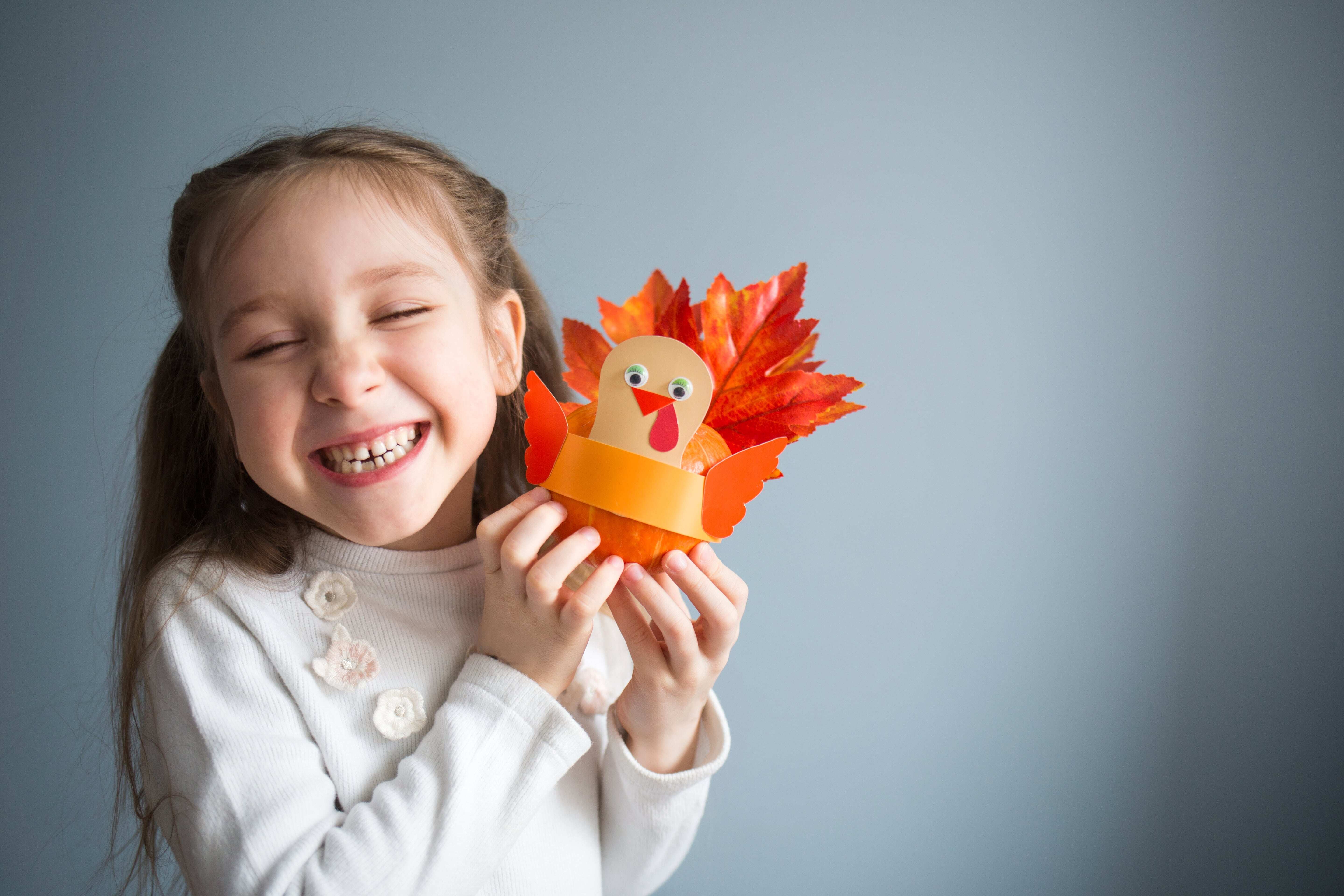 A young girl smiling and holding her craft turkey. 