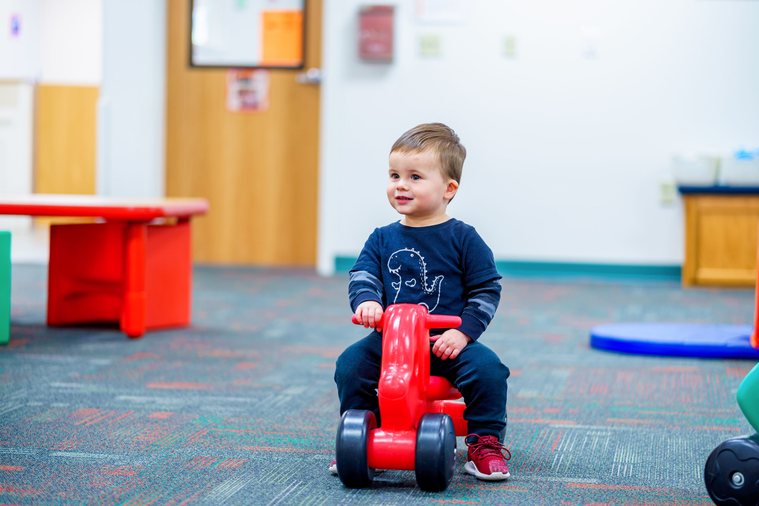 Older infant riding a push bike in the indoor play area