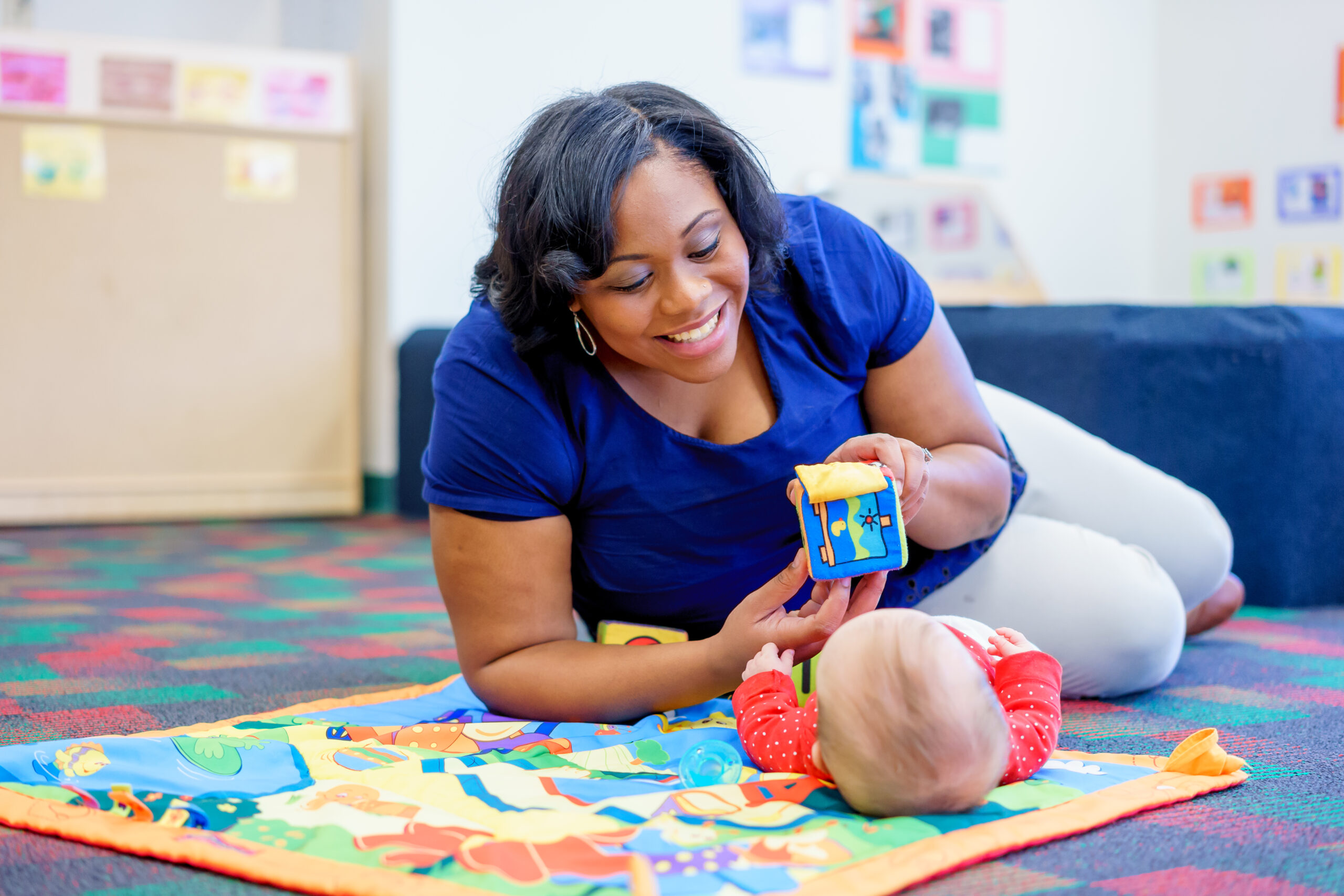 Teacher holding a soft block and playing with an infant on an activity mat
